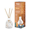 Ein Bolsius Raumduft-Diffuser mit Haselnuss-Vanille-Duft. Neben dem Diffuser steht die dekorative Verpackung des Artikels mit weihnachtlichem Motiv.