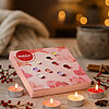 Eine rosafarbene Geschenkbox mit Duft-Teelichtern von Bolsius liegt auf einem Holztisch. Darum brennen mehrere Teelichter, dekoriert mit roten Beeren, Zimtstangen und Sternanis. Im Hintergrund sorgen Lichter für gemütliche Stimmung.