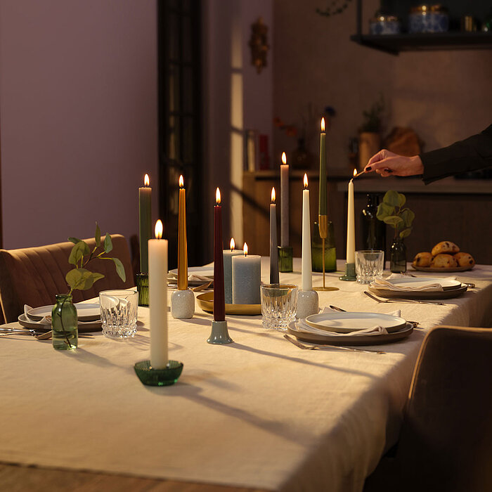 Eine durchgefärbte XL Rustik Haushaltskerze mit konischem Fuß in der Farbe Weiche Perle. Im Hintergrund ist ein 9er Pack der Stabkerzen in einer Schachtel von Bolsius zu sehen.