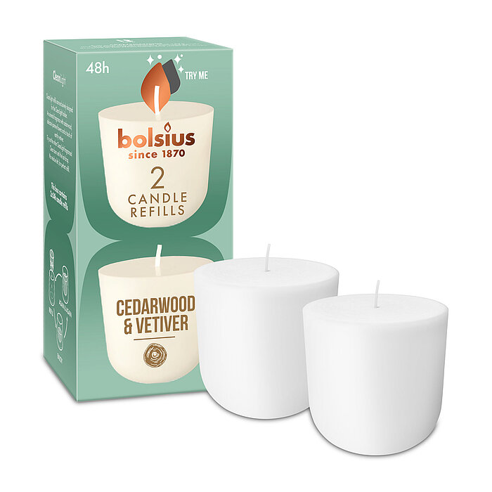 Zwei Cleanlight Duftkerzen-Nachfüller mit Zedernholz/Vetiver-Duft stehen neben der dazugehörigen grünen Verpackung mit Bolsius Schriftzug.