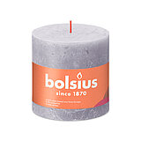 Eine durchgefärbte Rustik Stumpenkerze in der Farbe Gefrorener Lavendel mit den Maßen 100/100mm (H/DM). Der Banderole kann man die Marke "Bolsius" sowie die Hinweise "25% pflanzenbasiertes EU-Wachs", "0% tierisches Fett" und "Ohne Palmöl" ablesen.