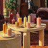 Stimmungsvolles Wohnambiente mit brennenden Bolsius Stumpen- & Rustik-Kerzen in warmen Farben auf modernen Beistelltischen.