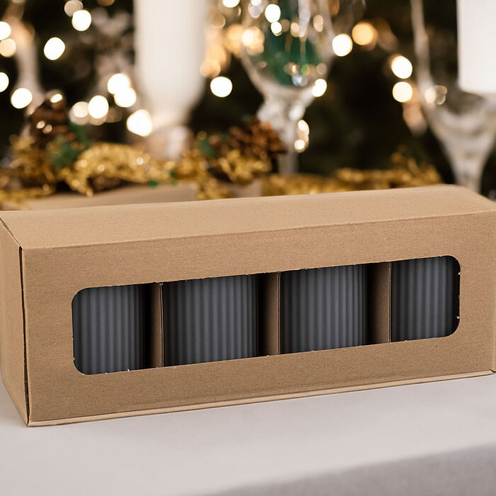 Eine geschlossene Verpackung mit fünf grauen gerippten Kerzen des Herstellers Wenzel steht auf einem festlich gedeckten Tisch. Im Hintergrund erhellen weiße Lichter eine dekorative Kulisse mit Gläsern, Tannenzapfen und goldenen Verzierungen. Die Atmosphär