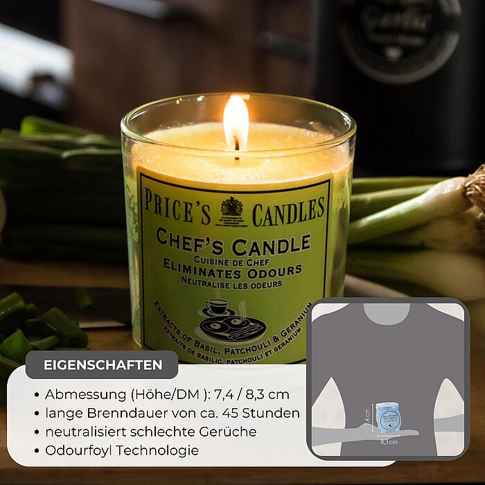 Ein brennendes Produkt von Price's Candles, eine Chef's Candle in einem transparenten Glas, steht auf einem Holzbrett in einer Küche. Umgeben ist die Kerze von frischen Zutaten, darunter eine rote Zwiebel, eine Knoblauchknolle, grüne Paprikastücke und Frü
