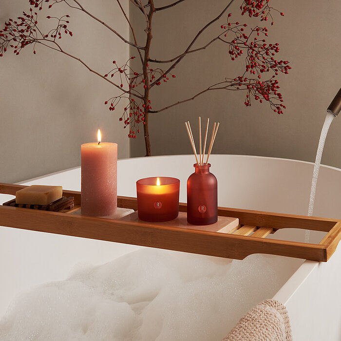 Eine entspannte Szene mit einer gemütlichen Badewanne. Auf einem Brett stehen Duftkerzen und Raumdüfte in romantischen Farbtönen.