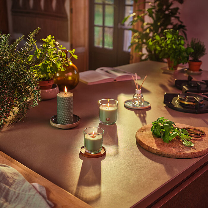 Rustikale Bolsius Rustik Stumpenkerze „Ribbed“ in der Farbe "Frische Olive", arrangiert neben Glas- und Duftkerzen auf Kerzentellern – schafft natürliche, gemütliche Wohnatmosphäre.