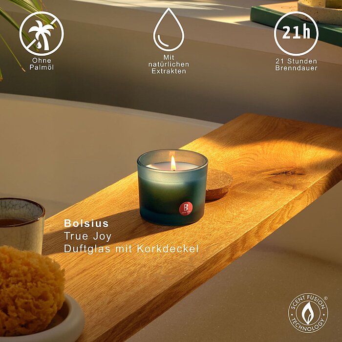 Eine Bolsius Duftglas True Joy aus blaugrünem Milchglas steht auf einem Holzbrett über einer Badewanne. Auf dem Bild sind Vorzüge der Kerze und die Brenndauer von 21h dargestellt.
