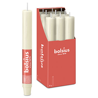 Eine durchgefärbte XL Rustik Haushaltskerze mit konischem Fuß in der Farbe Weiche Perle. Im Hintergrund ist ein 9er Pack der Stabkerzen in einer Schachtel von Bolsius zu sehen.