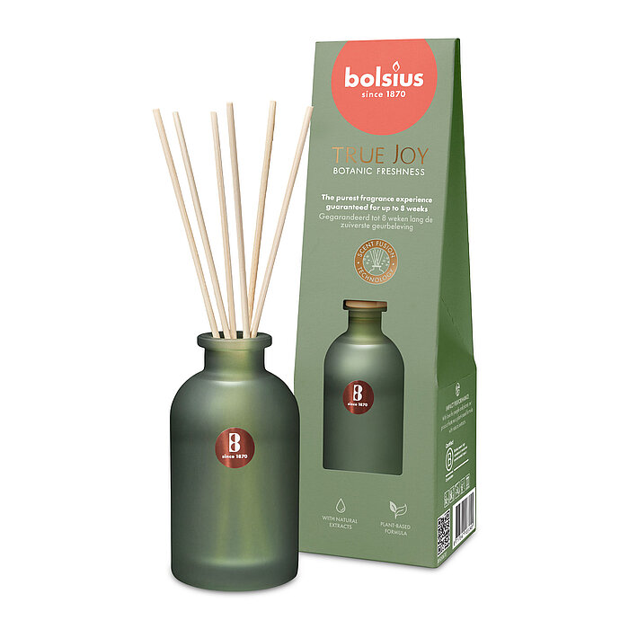 Ein Raumduft-Diffuser mit Rattanstäbchen aus grünem Milchglas mit der Duftrichtung "Botanic Freshness". Im Hintergrund ist die Verpackung des Artikels mit Bolsius Schriftzug zu sehen.