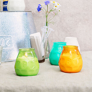 Bunte Outdoor-Kerzen in windfesten Gläsern (Grün, Orange, Gelb, Türkis) sorgen auf der Sommerterrasse für stimmungsvolle, gesellige Atmosphäre bei Drinks und Snacks.