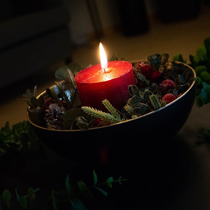 Goldene und silberne Weihnachtsdekorationen, darunter Kugeln, Sterne und eine Zapfen, liegen dekorativ auf einem mattschwarzen Hintergrund. Goldene und silberne Bänder schlängeln sich zwischen den Ornamenten und verleihen der Szene einen festlichen Glanz.
