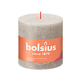 Eine durchgefärbte Rustik Stumpenkerze in der Farbe Sandgrau mit den Maßen 100/100mm (H/DM). Der Banderole kann man die Marke "Bolsius" sowie die Hinweise "25% pflanzenbasiertes EU-Wachs", "0% tierisches Fett" und "Ohne Palmöl" ablesen.