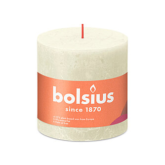 Eine durchgefärbte Rustik Stumpenkerze in der Farbe Weiche Perle mit den Maßen 100/100mm (H/DM). Der Banderole kann man die Marke "Bolsius" sowie die Hinweise "25% pflanzenbasiertes EU-Wachs", "0% tierisches Fett" und "Ohne Palmöl" ablesen.