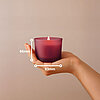 Eine Hand, die ein Bolsius Duftkerzenglas aus pinkem Milchglas hält. Das Bild steht die Größe der Kerze von 66/83mm dar.