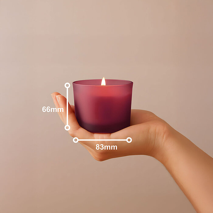 Eine Hand, die ein Bolsius Duftkerzenglas aus pinkem Milchglas hält. Das Bild steht die Größe der Kerze von 66/83mm dar.