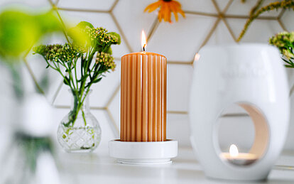Eine Duftkerze als Stumpenkerze steht auf einem schön dekorierten Tisch mit Vase und Teelicht.